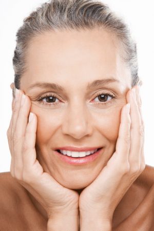 Closeup portrait of happy middle aged woman with hands on face over white background